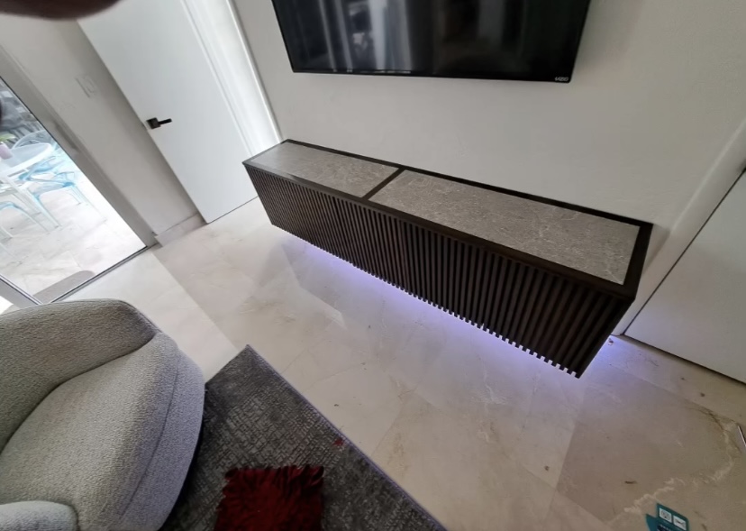 Wall-mounted dark slatted media console with stone-look top and concealed lighting