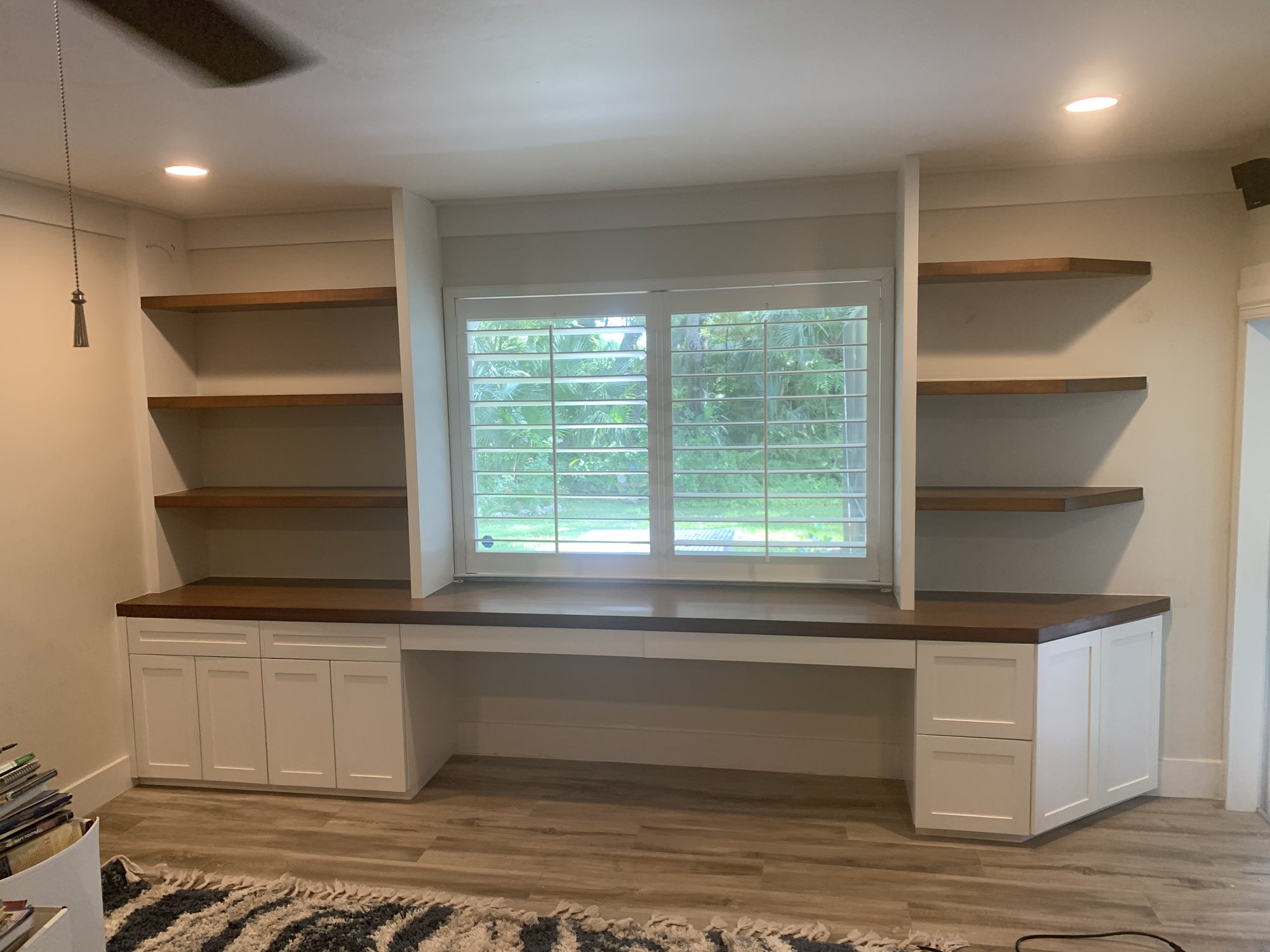 White built-in desk, cabinets, and wood shelves surrounding a window
